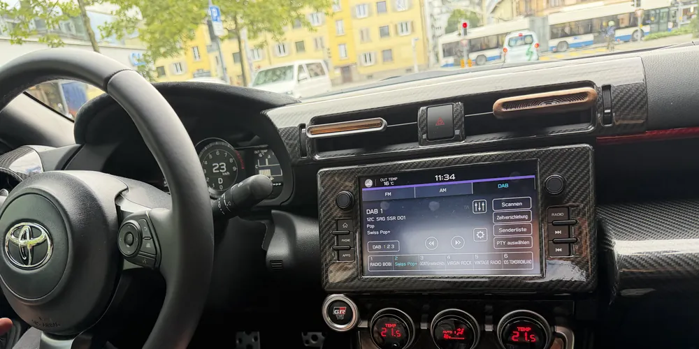 Blick vom Beifahrersitz auf Lenkrad, Tacho und Bildschirm eines Autos; durch die Frontscheibe eine Strasse in Luzern mit einem Trolleybus.