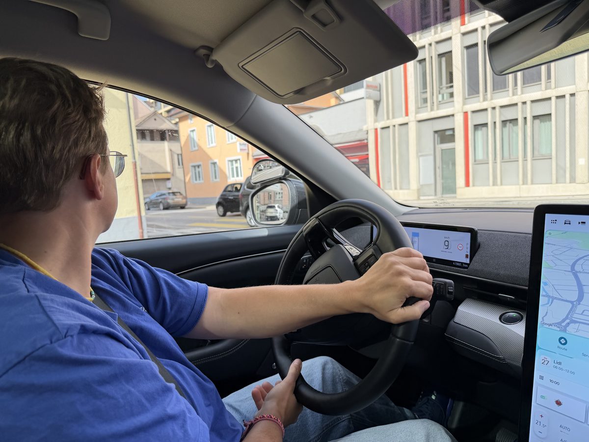 Fahrschüler mit beiden Händen am Lenkrad eines Fahrschulautos, Blick nach links an einer Kreuzung, der Fahrlehrer auf dem Beifahrersitz.